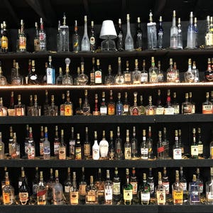 May include: A collection of glass bottles with lights inside, arranged on shelves. The bottles are various shapes and sizes, and some have labels. The bottles are illuminated from within, creating a warm glow.