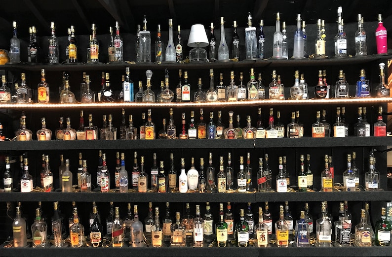 May include: A collection of glass bottles with lights inside, arranged on shelves. The bottles are various shapes and sizes, and some have labels. The bottles are illuminated from within, creating a warm glow.