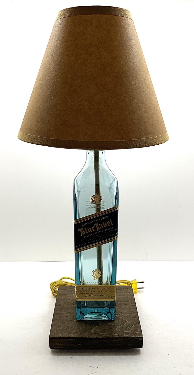 K&ouml;nnte beinhalten: Eine einzigartige Tischlampe aus einer recycelten Johnnie Walker Blue Label Whiskyflasche. Die Lampe hat einen blauen Glasflaschenfu&szlig;, einen braunen Lampenschirm und einen Holzsockel. Die Lampe ist eine dekorative Leuchte.