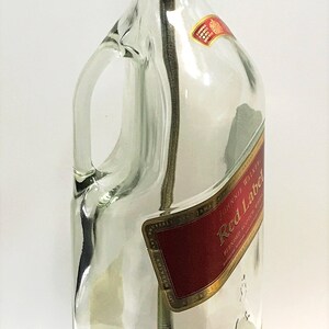 Puede incluir: Una l&aacute;mpara de botella de vidrio transparente con una pantalla dorada y una base de madera. La botella tiene una etiqueta que dice "Johnnie Walker Red Label Blended Scotch Whisky Established 1820 1.75 Litre".