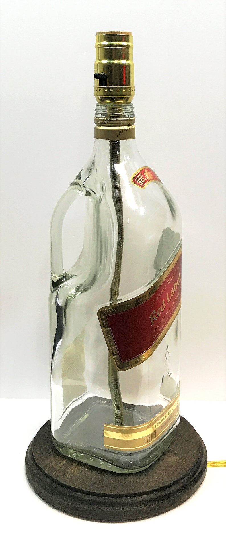 Puede incluir: Una l&aacute;mpara de botella de vidrio transparente con una pantalla dorada y una base de madera. La botella tiene una etiqueta que dice "Johnnie Walker Red Label Blended Scotch Whisky Established 1820 1.75 Litre".