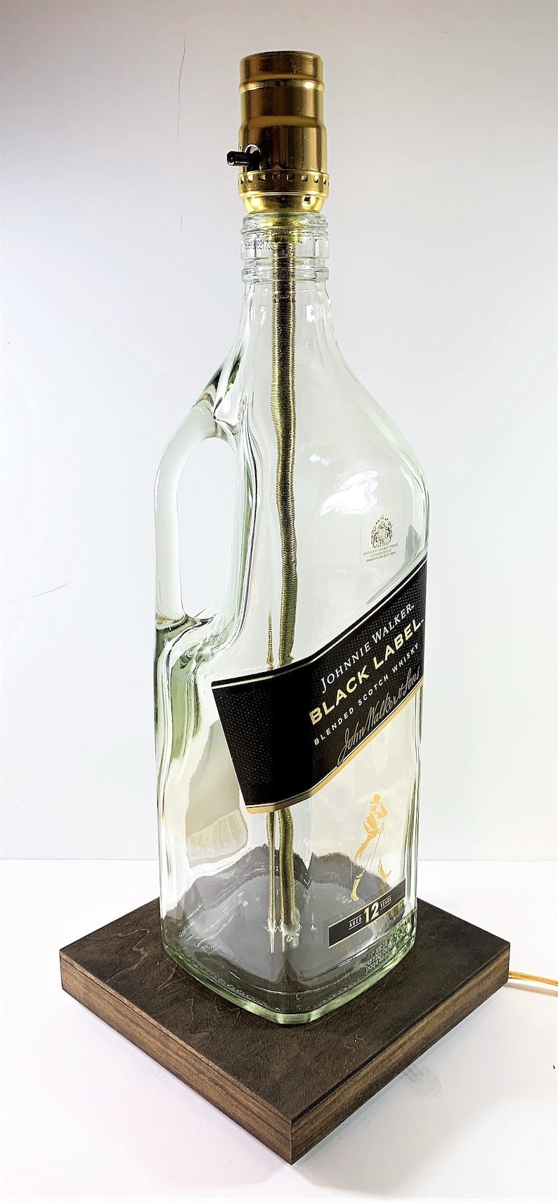 May include: A table lamp made from a repurposed Johnnie Walker Black Label bottle with a gold-colored lampshade and a wooden base.