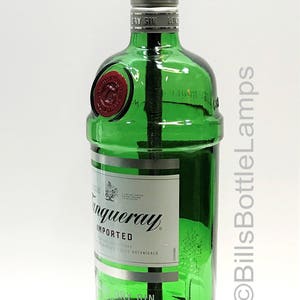 May include: A green glass bottle lamp with a gold light socket and a wooden base. The bottle is labeled "Tanqueray Imported London Dry Gin" and has a red seal on the side. The base is a dark brown oval shape.