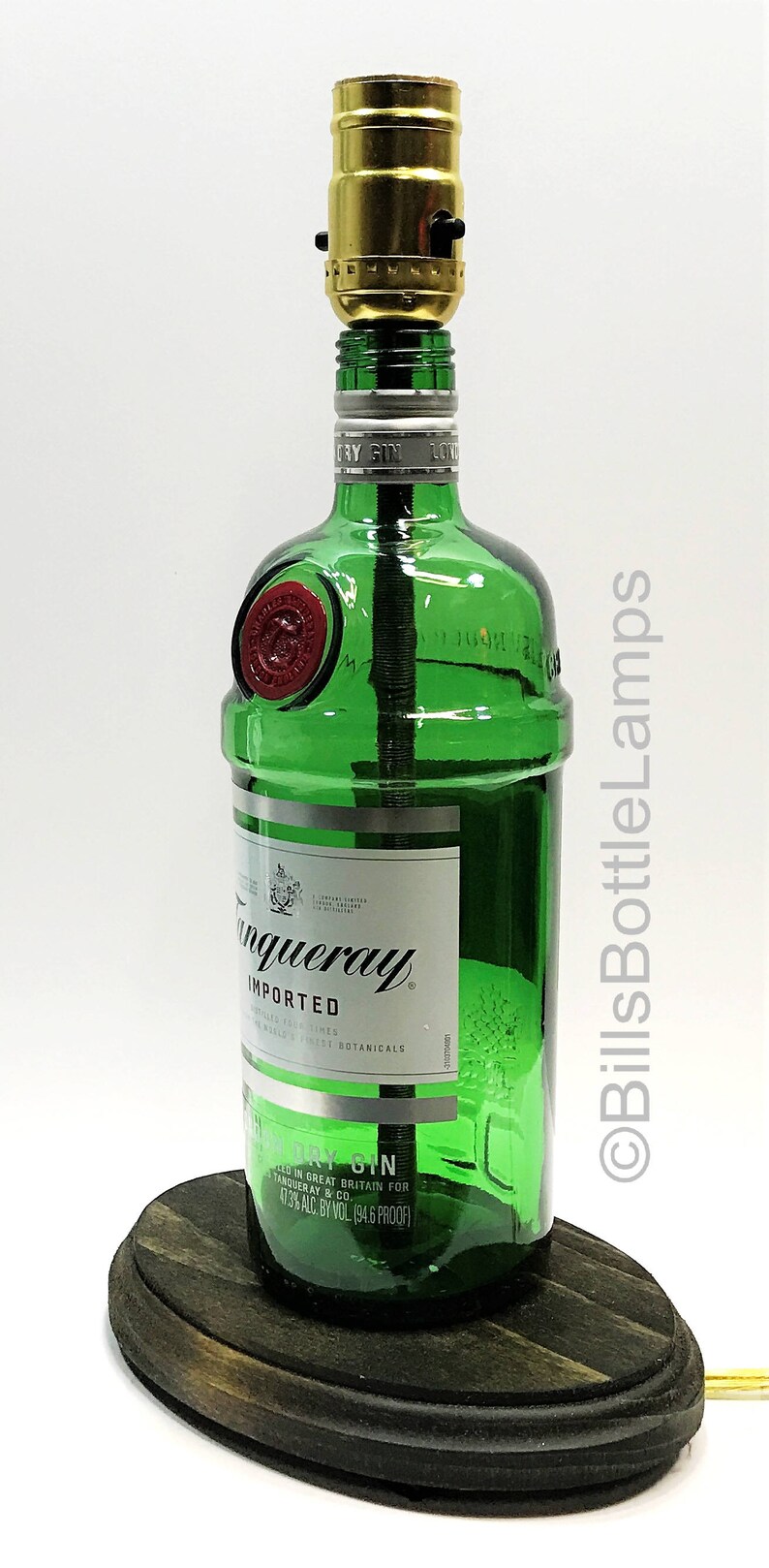 May include: A green glass bottle lamp with a gold light socket and a wooden base. The bottle is labeled "Tanqueray Imported London Dry Gin" and has a red seal on the side. The base is a dark brown oval shape.