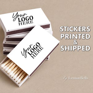 May include: A stack of white matchboxes with dark brown striking strips, featuring the black text "YOUR LOGO HERE" on the top surface. One open matchbox reveals wooden matches with white tips. The text "STICKERS PRINTED & SHIPPED" appears nearby.