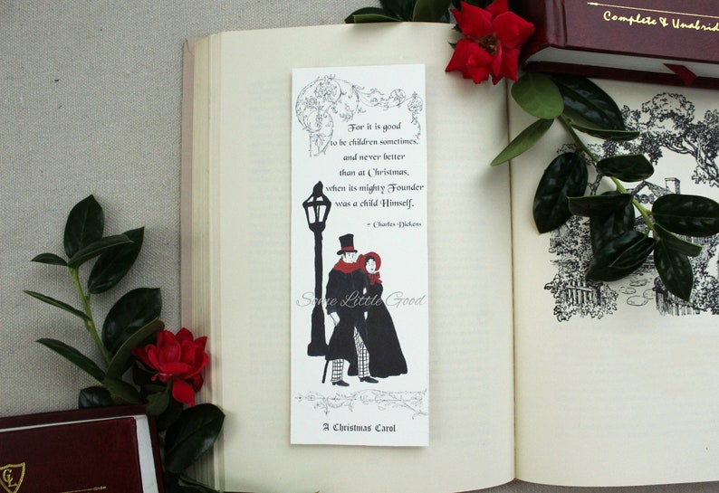 Pode incluir: Um marcador de p&aacute;gina branco com uma ilustra&ccedil;&atilde;o em preto e branco de um casal caminhando sob um poste de luz. O marcador de p&aacute;gina tem uma cita&ccedil;&atilde;o de A Christmas Carol de Charles Dickens: "Porque &eacute; bom ser crian&ccedil;a &agrave;s vezes e nunca melhor do que no Natal, quando o seu poderoso Fundador era uma crian&ccedil;a Ele mesmo." O marcador de p&aacute;gina tamb&eacute;m tem o texto "A Christmas Carol" e "Some Little Good" impresso nele.