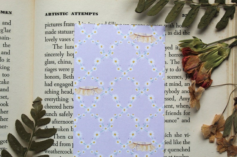 May include: A purple bookmark with a white daisy pattern. The bookmark has a white lace trim and the text "215" is written on the lace.