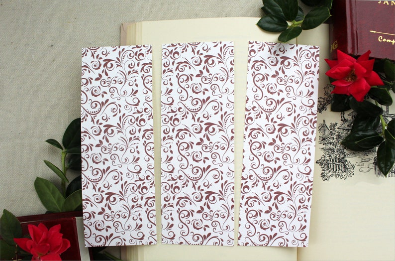 Pode incluir: Tr&ecirc;s cart&otilde;es de marcador de p&aacute;gina brancos com um padr&atilde;o floral castanho. Os marcadores de p&aacute;gina s&atilde;o retangulares e t&ecirc;m um fundo branco com um padr&atilde;o floral castanho.