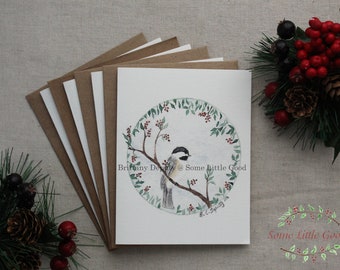 May include: A set of six blank greeting cards featuring a watercolor illustration of a chickadee perched on a branch with red berries. The illustration is surrounded by a wreath of green leaves and red berries. The text "Brittany Devault @ Some Little Good" is printed below the illustration.