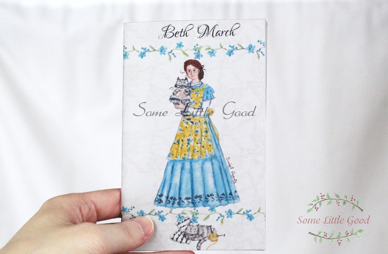 May include: A watercolor illustration of a woman named Beth March holding two kittens. The woman is wearing a blue dress with a yellow floral apron. The text "Some Little Good" is written in cursive at the top of the image and again at the bottom in a wreath of green leaves and red berries.
