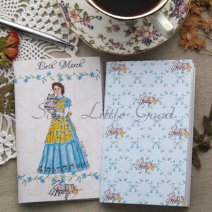 May include: Two small notebooks with a blue and white floral pattern. The front cover of one notebook features a watercolor illustration of a woman in a blue dress holding two kittens. The text "Beth March" is printed on the front cover of the notebook.