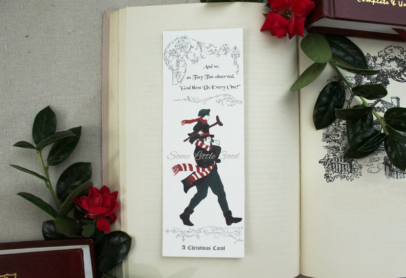 Pode incluir: Um marcador de p&aacute;gina branco com uma ilustra&ccedil;&atilde;o em preto e branco de um homem carregando uma crian&ccedil;a nos ombros. O marcador de p&aacute;gina tem o texto "And so, as Tiny Tim observed, 'God bless Us Every One!'". O marcador de p&aacute;gina tamb&eacute;m tem o texto "Some Little Good" e "A Christmas Carol".