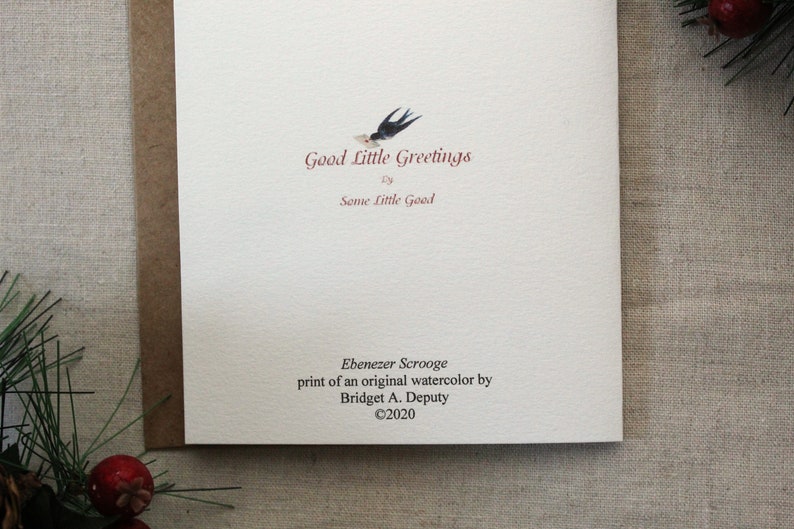 Pu&ograve; includere: Un biglietto di auguri con il testo "Good Little Greetings" e una piccola illustrazione di un uccello. Il biglietto include anche il testo "Ebenezer Scrooge" e il nome dell'artista, Bridget A. Deputy, con un avviso di copyright.