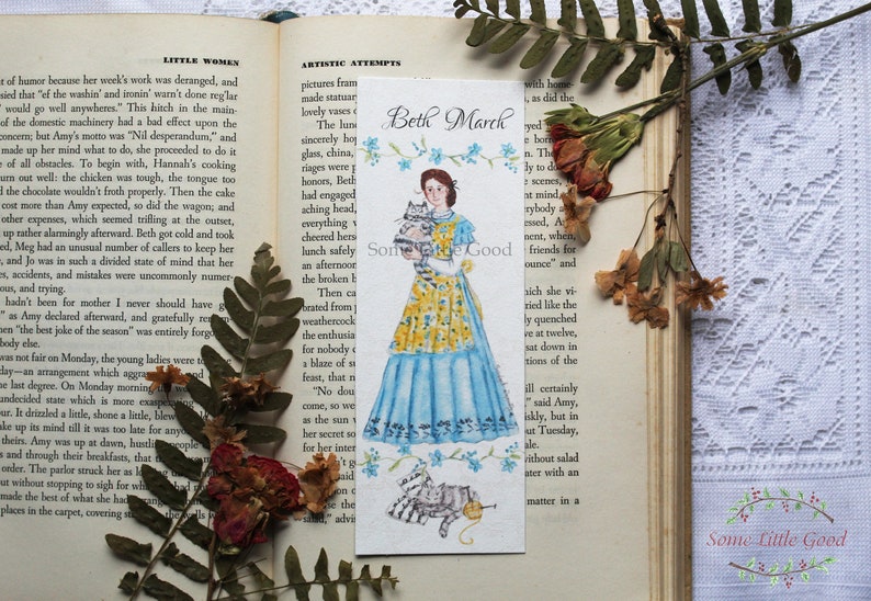 May include: A watercolor bookmark featuring a painting of Beth March from Little Women, holding two kittens. The bookmark is white with blue and yellow floral accents. The text "Beth March" is written in black at the top of the bookmark.