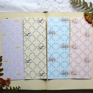 May include: Four different patterned bookmark designs. The bookmarks are all rectangular and feature a variety of floral and geometric patterns. The bookmarks are arranged in a row on a book.