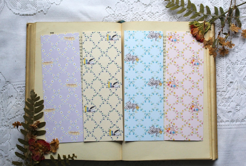 May include: Four different patterned bookmark designs. The bookmarks are all rectangular and feature a variety of floral and geometric patterns. The bookmarks are arranged in a row on a book.