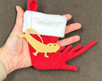 May include: A red felt stocking with a white cuff and a gold paper cutout of a lizard hanging from it.