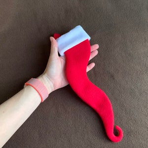 May include: A red and white felt stocking with a curled toe. The stocking is held in a hand.