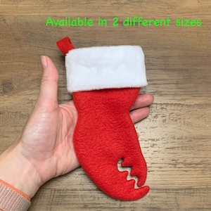 May include: Red and white felt Christmas stocking shaped like a crab claw. The stocking has a white cuff and a red felt claw.