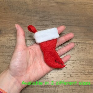 May include: A red felt stocking shaped like a crab claw with a white faux fur cuff. The stocking has a loop at the top for hanging.