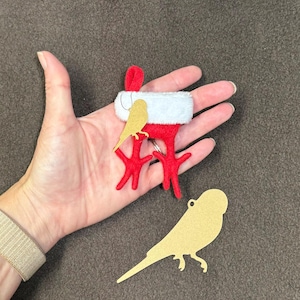May include: A red felt Christmas ornament shaped like a bird wearing a white fur hat. The ornament is holding a small yellow felt bird in its beak. A gold felt bird silhouette is also shown in the image.