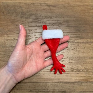May include: A red felt stocking with a white cuff, shaped like a hand with fingers. The stocking is held in a hand.