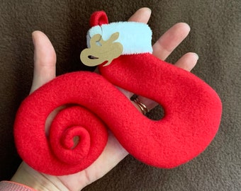 May include: A red felt stocking with a white cuff and a brown tag that says "Love" is curled into a spiral shape.