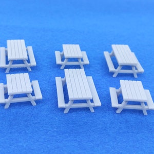 May include: Six miniature white wooden picnic tables with benches on a blue background.