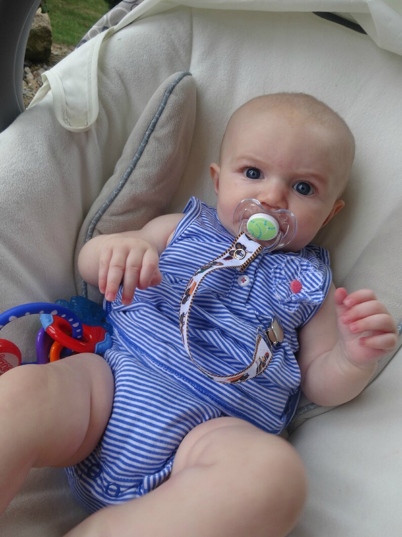 May include: A baby wearing a blue and white striped onesie with a pacifier in their mouth. The baby is sitting in a white and gray baby seat.