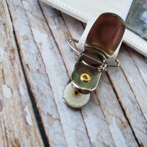 May include: A silver metal clip with a white plastic wheel. The clip is attached to a white fabric strap with the word "Science" embroidered on it.