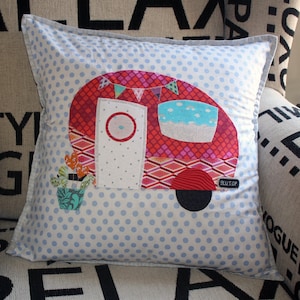 Op de afbeelding: Een blauw en wit gestippeld kussen met een rode, roze en witte camper-applicatie. De camper heeft een witte deur met een blauw raam en de tekst "BUILT UP" aan de zijkant.