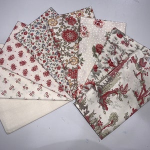May include: A set of eight fabric squares in various patterns. The fabric is a cream colour with red and green floral designs. The fabric squares are arranged in a fan shape.