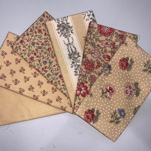 May include: A selection of folded fabric squares with floral and patterned designs. The fabrics display a palette of beige, red, blue, and cream. The patterns include floral prints, polka dots, and a striped design with a tree motif.