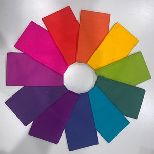 Pode incluir: Um conjunto de dez amostras de tecido em várias cores, incluindo roxo, rosa, azul, verde, amarelo, laranja e vermelho. As amostras estão dispostas em um círculo.