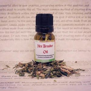 May include: A small glass bottle with a black cap and a brown label that reads "Hex Breaker Oil". The bottle is sitting on a pile of dried herbs.