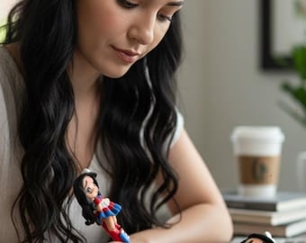 May include: A red ballpoint pen featuring a small doll topper with black hair, a white top, and a blue and red skirt. The pen barrel displays a small Puerto Rican flag emblem. Text on the image reads: You can customize the doll, Customize your name.