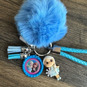 May include: A blue fuzzy keychain with a blue and pink Frozen character charm, a silver ring, and blue tassels. The charm features Elsa and Anna from the movie Frozen.
