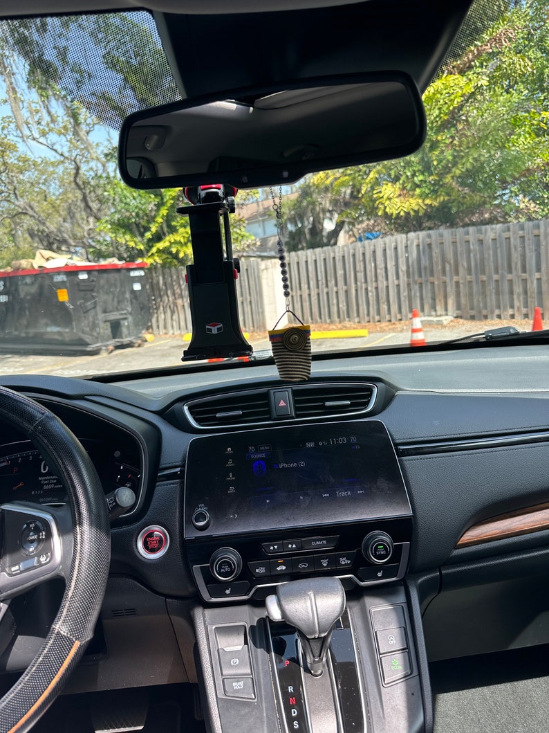 May include: The interior of a black car with a black steering wheel, a black dashboard, and a black gear shift. The car has a digital display screen that says "iPhone (2)" and "Track". There is a red button on the dashboard that says "Start/Stop".