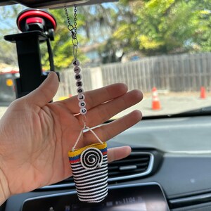 May include: A car air freshener with a black and white striped fabric bag hanging from a chain with white beads that spell "COLOMBIA".