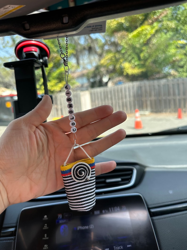 May include: A car air freshener with a black and white striped fabric bag hanging from a chain with white beads that spell "COLOMBIA".