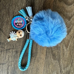May include: A blue fuzzy keychain with a braided blue strap, a small plastic doll, and a round charm with a picture of two girls.