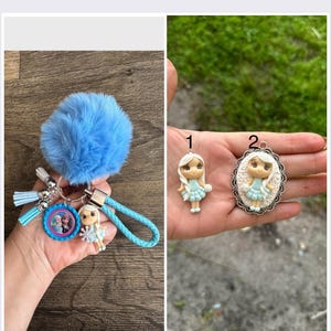 May include: A blue fuzzy keychain with a silver key ring, a blue charm with a picture of two girls, a small blue doll charm, and a blue braided cord. There are two other charms, one with a blue doll and the other with a blue doll in a silver oval frame.