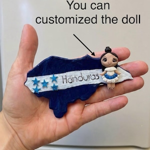 May include: A handcrafted Honduras-shaped ornament in blue and white, featuring five blue stars and the word "Honduras." A small doll in a white and blue dress is attached. The text "You can customized the doll" is also present.