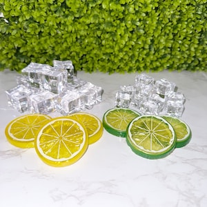 May include: A close-up of a white surface with two piles of clear ice cubes and three yellow lemon slices and three green lime slices.