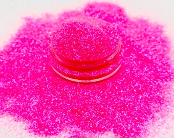 May include: A close-up of a pink glitter, with a small sample of the glitter in a clear container.