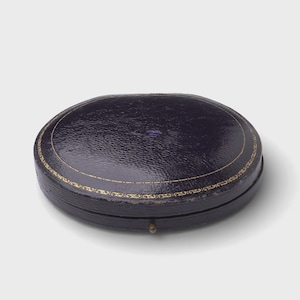 Puede incluir: Taza de cerámica blanca con asa negra y la frase "But First, Coffee" en negro. El fondo borroso sugiere un ambiente acogedor.