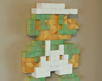 May include: A pixelated figure of a video game character made from wooden blocks. The figure is green, white, and brown. The figure is mounted on a wall.