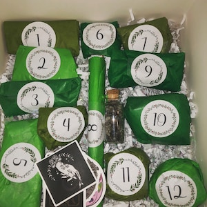 May include: An advent calendar box filled with wrapped green packages, numbered 1 through 12, with white circular labels and a wreath design. A glass bottle with a cork stopper and a few tarot cards are also visible.