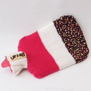 May include: A knitted hot water bottle cover with a brown, white and pink striped design. The top of the cover has a brown label with the text "URFAB" in yellow letters.