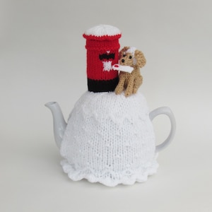 Può includere: Coperta per teiera in maglia bianca con una cassetta delle lettere rossa e nera e un piccolo cane di maglia marrone in cima.